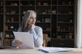 Attractive brooding aged businesswoman holds papers sit at workplace desk