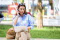 Attractive brown-haired woman is sitting on a bench in the street and using laptop and mobile phone for work Royalty Free Stock Photo