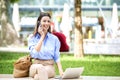 Attractive brown-haired woman is sitting on a bench in the street and using laptop and mobile phone for work Royalty Free Stock Photo