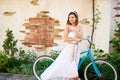 Attractive brunette girl posing near blue bike in front of old brick building. Royalty Free Stock Photo