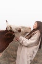 Attractive brunette girl in white coat blows a kiss to a cow, meadow in fog on the background Royalty Free Stock Photo