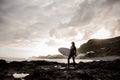 Attractive brunette man standing in the black swimsuit with a white surf in his hands on the shore Royalty Free Stock Photo