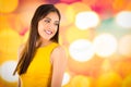 Attractive brunette wearing yellow dress posing naturally and smiling beautiful to camera with blurry colorful Royalty Free Stock Photo