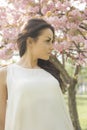 Attractive brunette woman in light dress looking at camera while posing near flowering tree Royalty Free Stock Photo