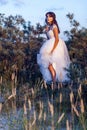 Attractive brunette woman with makeup and hairstyle wearing white wedding dress while posing at glade. holding her dress and Royalty Free Stock Photo