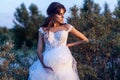 Attractive brunette woman with makeup and hairstyle wearing white wedding dress while posing at glade. looking away with hand on Royalty Free Stock Photo