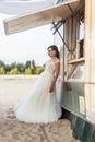 Attractive brunette woman with makeup and hairstyle wearing white wedding dress while posing and lean near street food car. Royalty Free Stock Photo