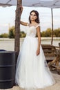 Attractive brunette woman with makeup and hairstyle wearing white wedding dress while posing outside. standing and looking at Royalty Free Stock Photo