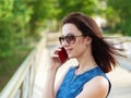 Attractive brunette woman in sunglasses and blue jeans dress has emotional phone conversation on mobile phone on park bridge outdo Royalty Free Stock Photo