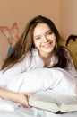 Attractive brunette young woman beautiful happy smiling student girl in bed with book looking at camera portrait Royalty Free Stock Photo