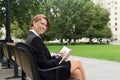 Attractive business woman sits on parks bench and writes in her Royalty Free Stock Photo