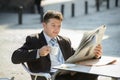 Attractive businessman sitting outdoors having coffee cup for breakfast early morning reading newspaper news looking relaxed Royalty Free Stock Photo