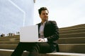 Attractive businessman wearing suit and using modern laptop outdoors. Successful banker working outside during break. Royalty Free Stock Photo