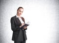 Attractive businesswoman in formal suit and shirt is holding a planner and pen, taking notes, looking straight camera and dreaming Royalty Free Stock Photo