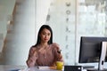 Attractive businesswoman holding pen and looking to camera while sitting in front of computer. Royalty Free Stock Photo