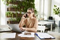 Attractive businesswoman making a call while sitting in front of laptop in the office and working Royalty Free Stock Photo