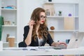 Attractive businesswoman sitting at desk in cozy bright office and working with laptop computer.