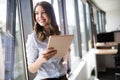 Attractive businesswoman using a digital tablet while standing in front of windows Royalty Free Stock Photo