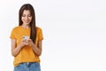 Attractive, carefree emotive young brunette woman in yellow t-shirt, holding smartphone smiling excited, looking mobile