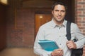 Mid-adult man standing on right in brick corridor, holding blue notebook, gripping backpack strap Royalty Free Stock Photo