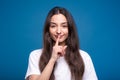 Attractive caucasian or arab brunette girl in white t-shirt showing silence gesture isolated on blue studio background. Royalty Free Stock Photo