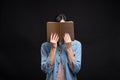 Attractive caucasian brunette girl in a shirt covering her face with a book and reading isolated on a black studio background. Royalty Free Stock Photo