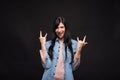 Attractive caucasian brunette girl in shirt happily screaming and showing rocker or punk gesture isolated on black studio backgrou