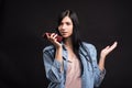 Attractive caucasian brunette girl in a shirt holding a smartphone in her hand and recording a voice message isolated on a black s Royalty Free Stock Photo
