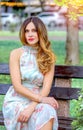 Attractive Caucasian girl sitting on a bench in the park. Light summer dress, floral print. Urban landscape. Royalty Free Stock Photo