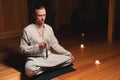 An attractive caucasian man in a lotus position sits in a dark meditation room and holds a red rosary for prayer in his Royalty Free Stock Photo