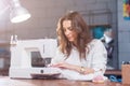 Attractive Caucasian seamstress working stitching with sewing machine at her workplace in studio loft interior Royalty Free Stock Photo
