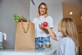 Attractive Caucasian woman in casual clothes giving apple to little girl in kitchen Royalty Free Stock Photo