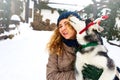 Attractive caucasian woman hugs funny malamute dog wearing santa dear christmas antlers. Curly smiling female having fun Royalty Free Stock Photo