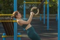 Attractive Caucasian woman pulls up on gymnastic rings during a workout on a street sports ground. Royalty Free Stock Photo