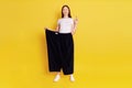 Attractive Caucasian young female wearing old huge pair of pants, weight loss, stands with close eyes, keeps fingers crossed, make