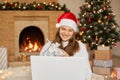 Attractive Caucasian young smiling girl in santa hat having video call on her Laptop while sitting on floor at home near christmas Royalty Free Stock Photo