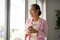 Attractive senior Asian businesswoman stands by the window with her coffee in her hands