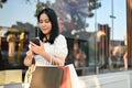 Asian woman with her shopping bags using her smartphone, standing in front of shopping mall Royalty Free Stock Photo