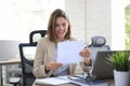 Attractive cheerful business woman checking paper documents in office, working on laptop Royalty Free Stock Photo