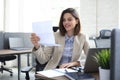 Attractive cheerful business woman checking paper documents in office, working on laptop Royalty Free Stock Photo