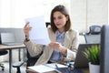 Attractive cheerful business woman checking paper documents in office, working on laptop Royalty Free Stock Photo