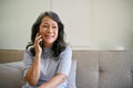 A middle-aged Asian woman enjoys talking on the phone with her friend on a sofa Royalty Free Stock Photo