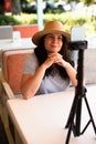 Attractive cheerful woman outside sitting with tripod and smartphone,making video call or providing online lesson.Vertical Royalty Free Stock Photo