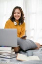 Attractive Asian woman remote working from home, using laptop on bed in her bedroom Royalty Free Stock Photo