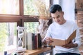 Cheerful young handsome man wearing white T-shirt reading books in his hands sitting on chair beside window at home. Royalty Free Stock Photo