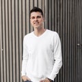 Attractive cheerful young man in a white stylish shirt with a cute smile is standing near a wooden vintage building in stripes