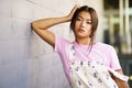 Attractive Chinese girl looking at camera with serious expression leaning against an urban wall Royalty Free Stock Photo