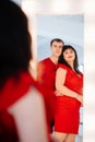 an attractive chubby woman in a red dress with a man looks in the mirror.
