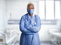 Attractive and confident black African American medicine doctor wearing face mask and blue scrubs standing corporate in health