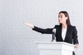 attractive, confident lecturer pointing with hand while standing on podium tribune.